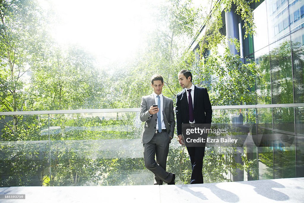 Two businessmen chatting surrounded by trees.