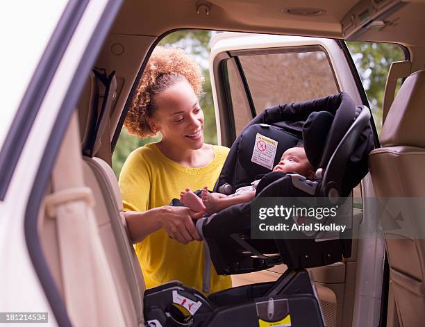 mixed race mother loading baby into car seat - car seat stock pictures, royalty-free photos & images
