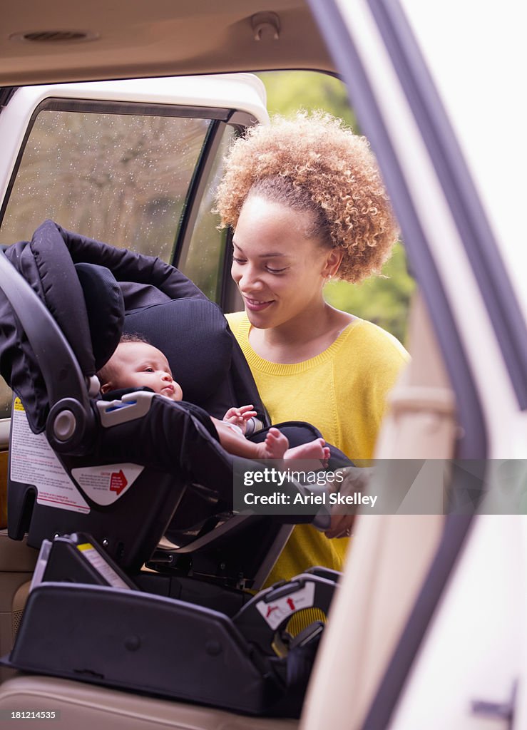 Mixed race mother loading baby into car seat