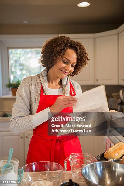 mixed race woman baking in kitchen - baking reading recipe stockfoto's en -beelden