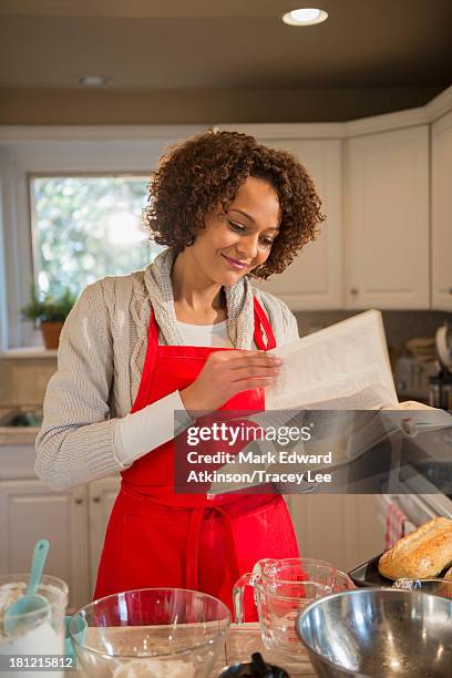 mixed race woman baking in kitchen - reading cookbook stock pictures, royalty-free photos & images