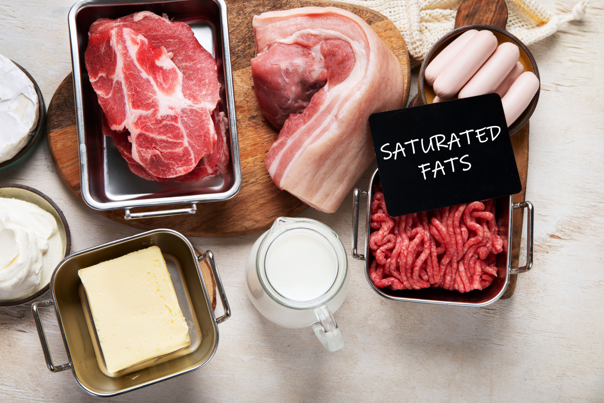 Saturated fats on tables. Raw meat, sausages, cheese, butter. Bad food concept Saturated fats on tables. Raw meat, sausages, cheese, butter. Bad food concept