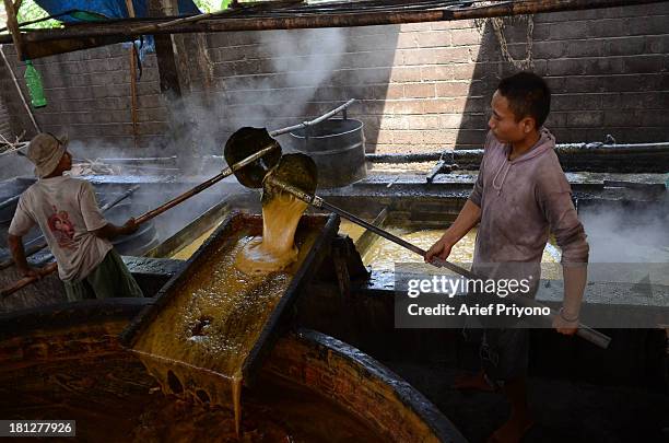 Worker supervising boiling vats of sugar cane juice while making brown sugar in a small factory in Slumbung village. Most Indonesian people use brown...