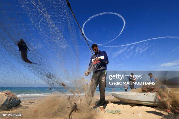 Palestinian fishermen sort their catch in Deir el-Balah, in the central Gaza Strip as contrails from an Israeli aircraft line the sky on November 30,...