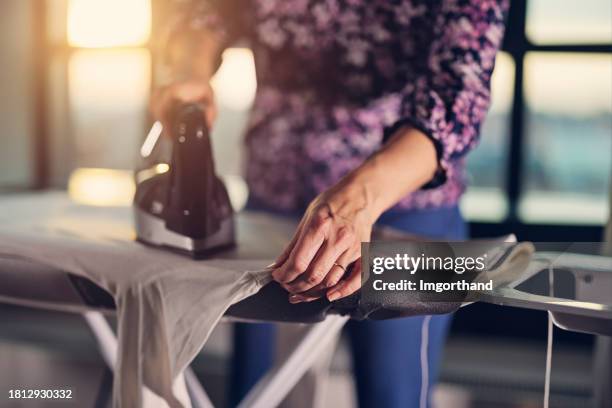 mother is ironing a white turtleneck blouse for a teenage daughter - alleen één oudere vrouw stockfoto's en -beelden