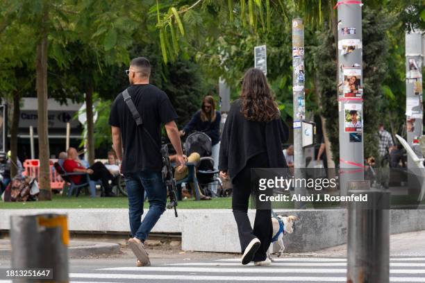 An off duty member of the Israeli security forces walks with a woman and a dog on Shabbat morning in Dizengoff Square on November 25, 2023 in Tel...
