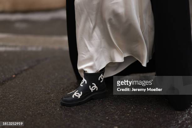 Karin Teigl seen wearing Mango cream white satin / silk long skirt, H&M black wool long coat and Chanel black / white logo pattern rubber boots, on...