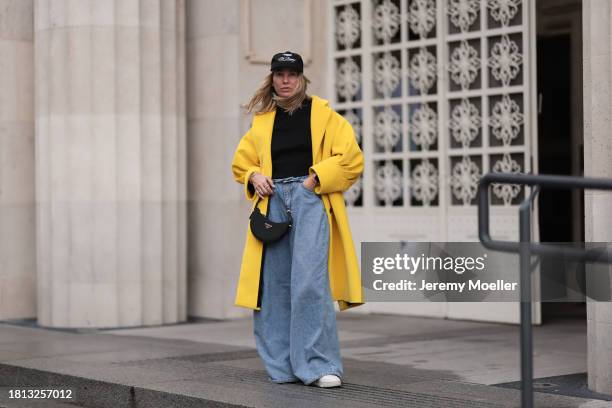 Karin Teigl seen wearing Cole Buxton black logo cap, Chanel black top, Prada yellow wool long oversized coat, The Frankie Shop light blue wide leg...