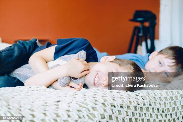 two brothers, 9 and 10 years old, lie on the bed and sleep with a smile on their faces, against the background of an orange wall - 10 11 years stock pictures, royalty-free photos & images