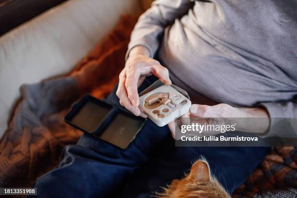 senior woman embracing modern technology: a heartwarming photo series showcasing an elderly woman opening a package with a new hearing aid at home - ear canal stock-fotos und bilder