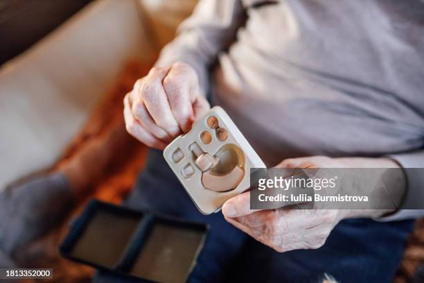 close-up of an elderly woman's hands holding and opening a box with a hearing aid, unpacking purchases - ear canal stock-fotos und bilder