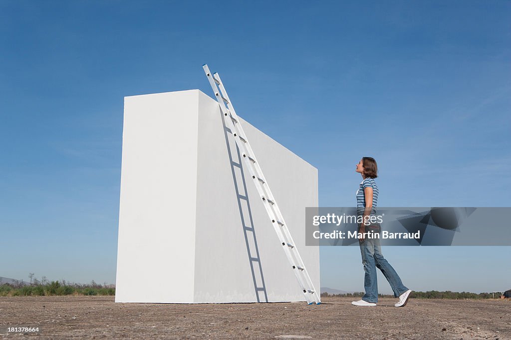 Femme à la recherche à l'échelle contre le mur à l'extérieur