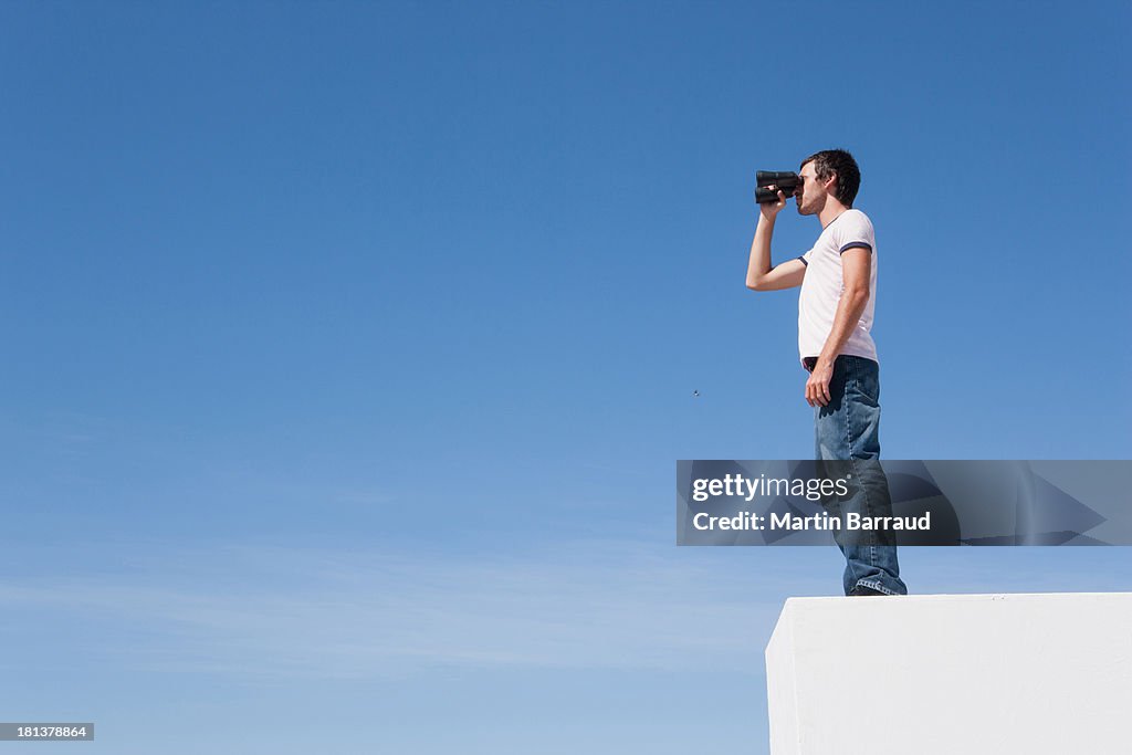 Man on pedestal with binoculars and blue sky outdoors