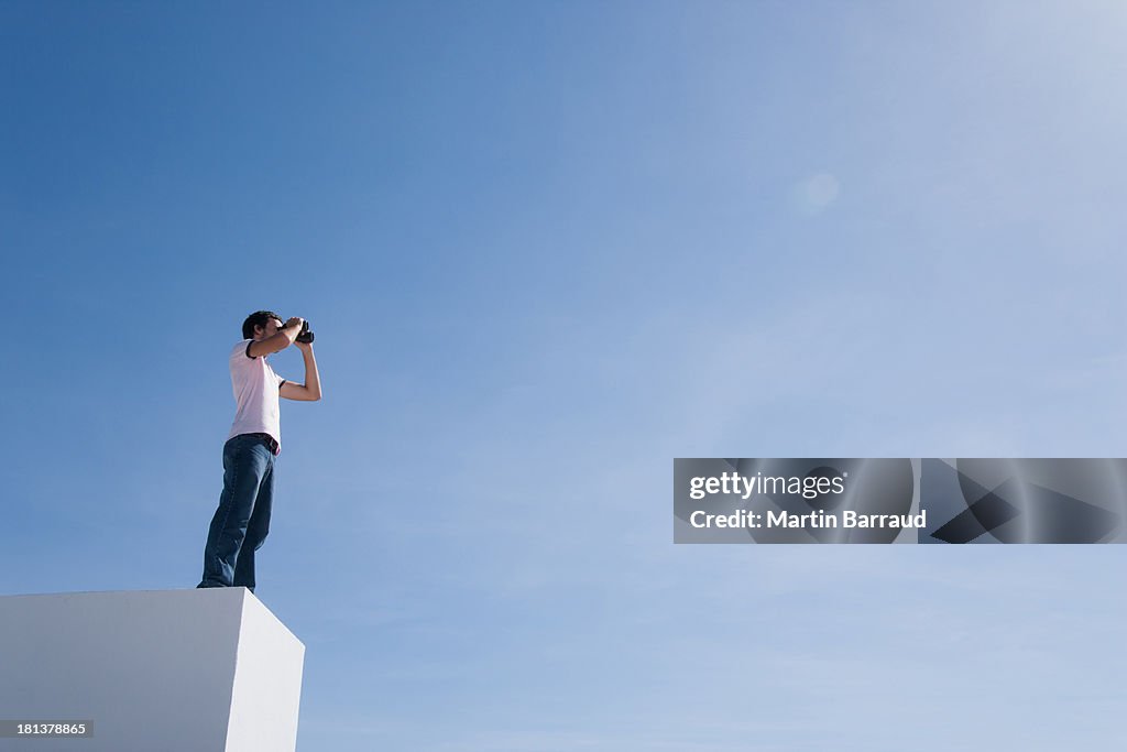 Man on pedestal with binoculars and blue sky outdoors