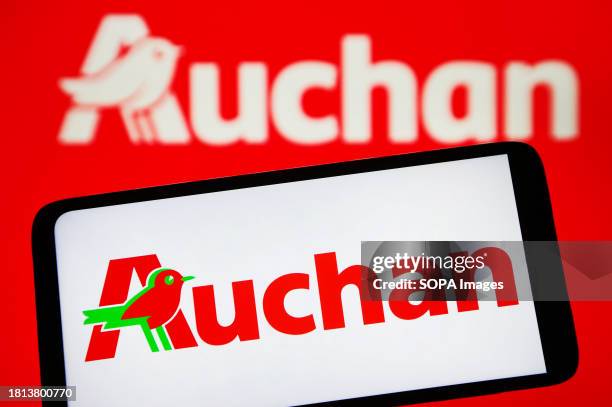 In this photo illustration, Auchan logo is seen on a smartphone and on a pc screen.