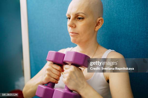 bald woman with breast cancer exercising with dumbbells at home - shaved head stock pictures, royalty-free photos & images