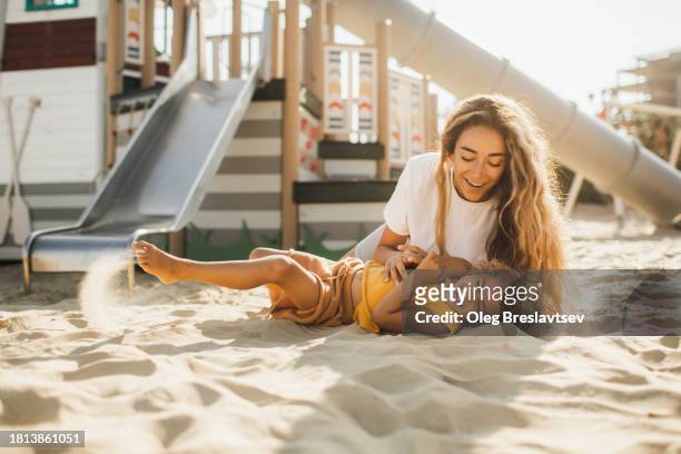 happy mom having fun with daughter in sand on beach playground. summer sunny day. happy motherhood - mothers day beach fotografías e imágenes de stock