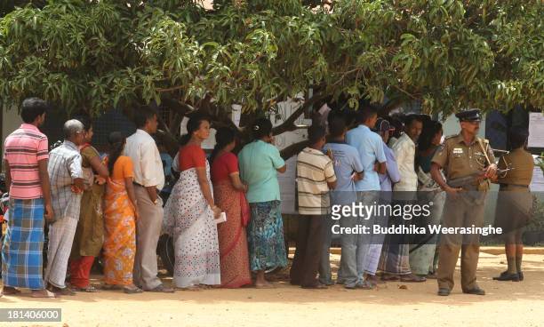 Sri Lankan ethnic Tamil people wait to vote as police officers stand guard at a polling station during the northern provincial council election on...