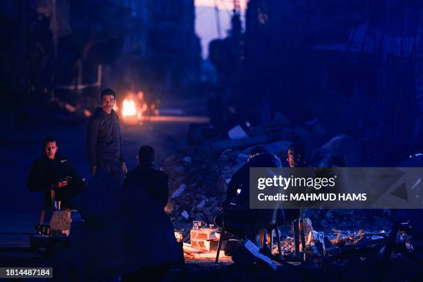 People sit around a camp fire in the midst of destroyed buildings in the Khezaa district on the outskirts of the southern Gaza Strip city of Khan...