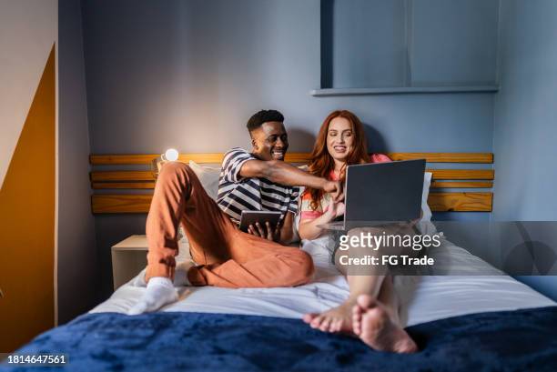 paar spricht und benutzt computer im schlafzimmer des hostels - man in suite holding tablet stock-fotos und bilder