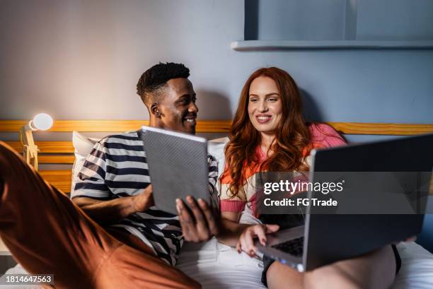 junger mann zeigt seiner frau etwas auf digitalem tablet im schlafzimmer des hostels - man in suite holding tablet stock-fotos und bilder