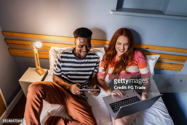 couple talking and using technologies in bedroom at hostel - man in suite holding tablet stockfoto's en -beelden