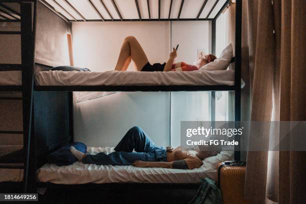 compañeros de piso descansando/usando el teléfono móvil en el albergue - litera fotografías e imágenes de stock