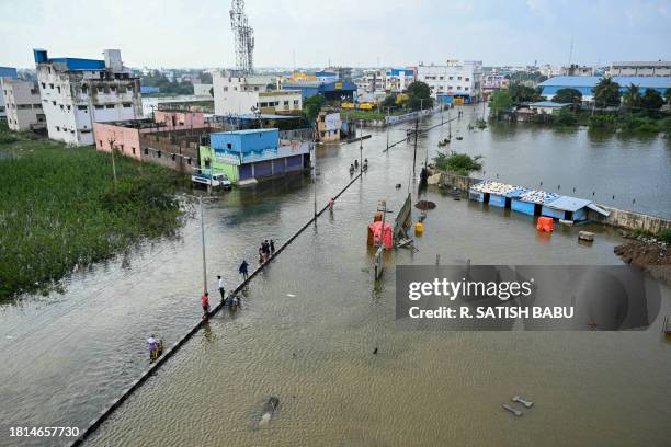 Commuters wade across a flooded street after heavy rains in Chennai on December 1, 2023.