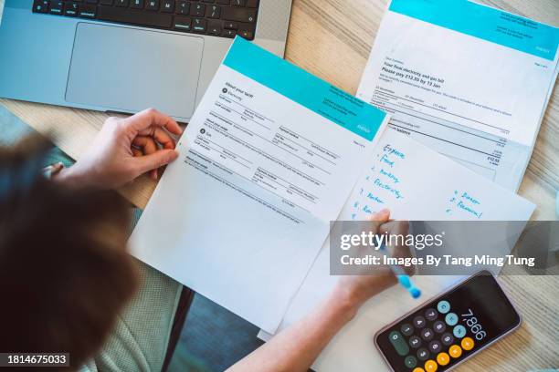 overhead view of young asian women managing home finance using laptop & smartphone. she is working with household utility bill and calculating expenses at home. - energy bill stock pictures, royalty-free photos & images
