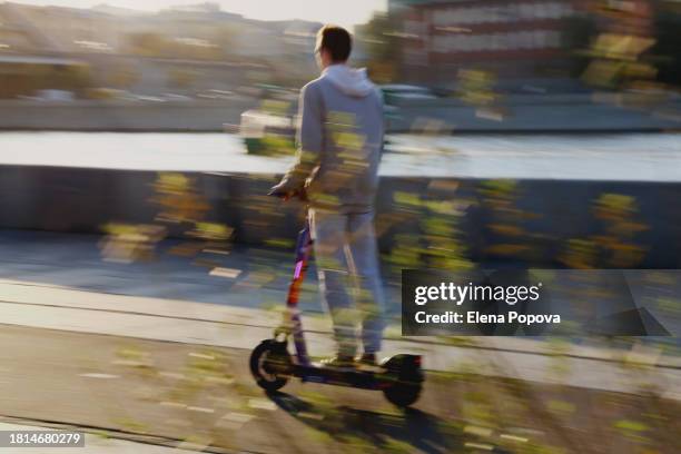 defocused city life background, unknown freelancer riding fast electric push scooter at the embankment - veicolo elettrico automobile con biodiesel foto e immagini stock