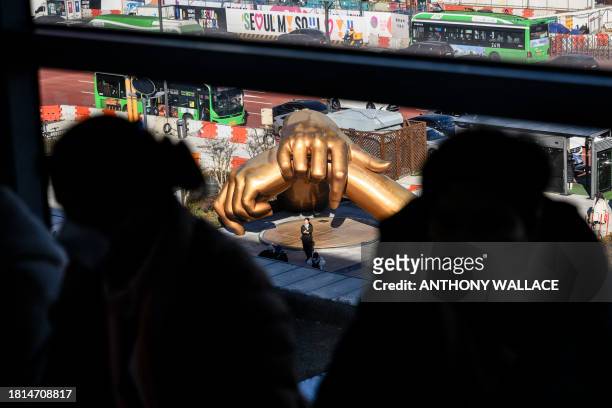 Visitors at a job fair for North Korean defectors sit next to a window with a view of a woman posing in front of a bronze sculpture by artist Hwang...