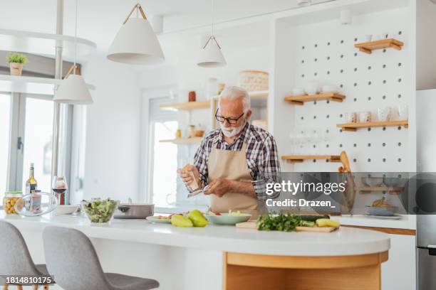 senior man in kitchen cooking healthy meal - mediterranean diet stockfoto's en -beelden
