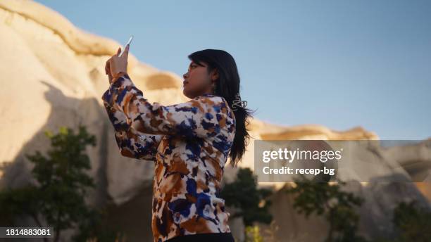 multiracial beautiful female tourist using her smart mobile phone to take photos and videos of nature and rock formation in cappadocia in türkiye turkey - göreme national park stock pictures, royalty-free photos & images