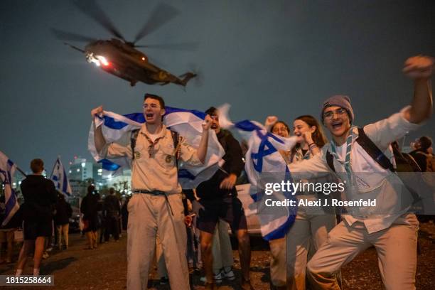 Israeli youth groups wave Israeli flags, sing, and dance as a second helicopter with Israeli hostages released earlier by Hamas lands at Schneider...