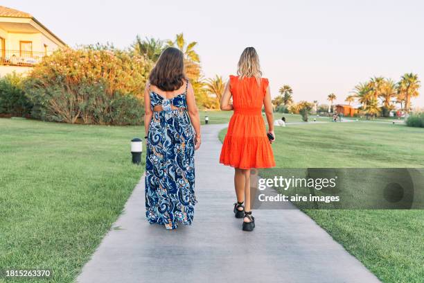 two women in dresses walking on a garden path with grass around them, rear view. - white dress back stock pictures, royalty-free photos & images