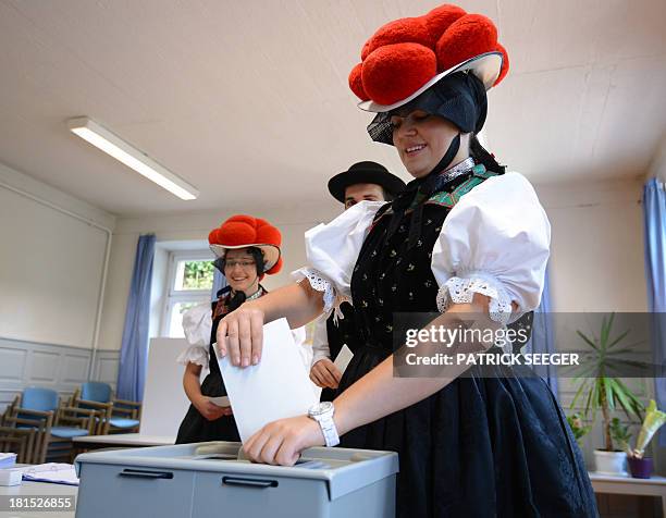 Voters Gerlinde Moser, Christoph Wöhrle and Corinna Wöhrle wear Black Forest traditional clothes and the pom-poms hat "Bollenhut" as they queue to...