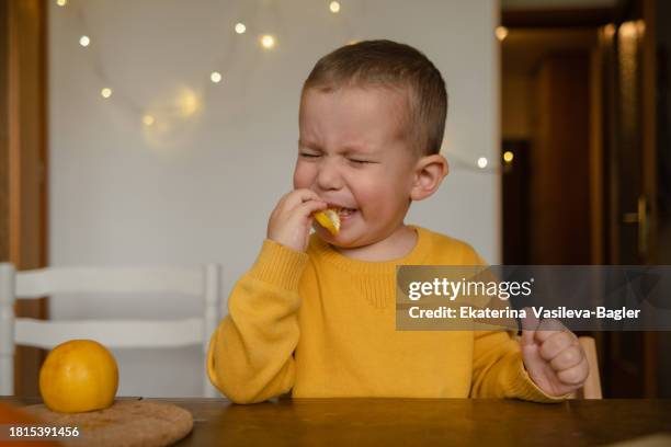 child eats sour lemon.little boy biting yellow lemon - baby sauer stock-fotos und bilder