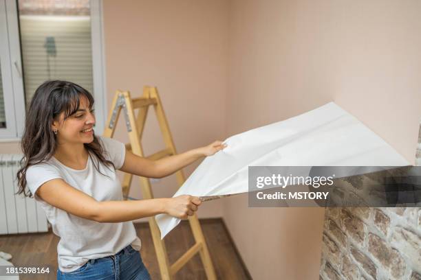 young girl takes the wallpaper off the wall before painting the wall. - vrouw behangen stockfoto's en -beelden