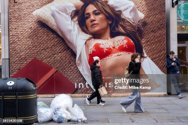 Shoppers and visitors out in Covent Garden pass a large scale hoarding featuring a photograph of American singer and actress Jennifer Lopez covering...