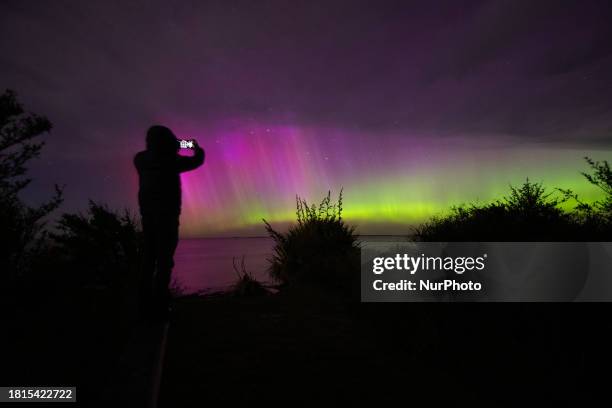 Man is taking pictures of the Aurora Australis as it illuminates the night sky above the waters of Lake Ellesmere on the outskirts of Christchurch,...