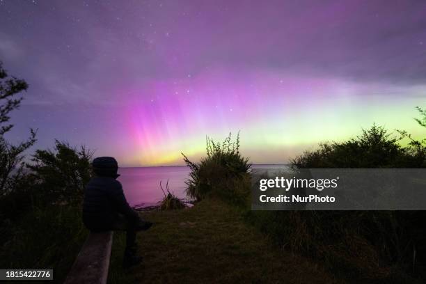 Man is looking at the Aurora Australis as it illuminates the night sky above the waters of Lake Ellesmere on the outskirts of Christchurch, New...