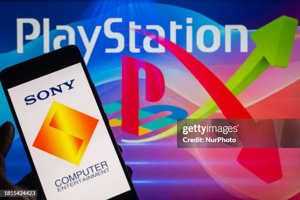 The Sony Interactive Entertainment logo is being displayed on a smartphone with a PlayStation and a stock graph visible in the background, in this...