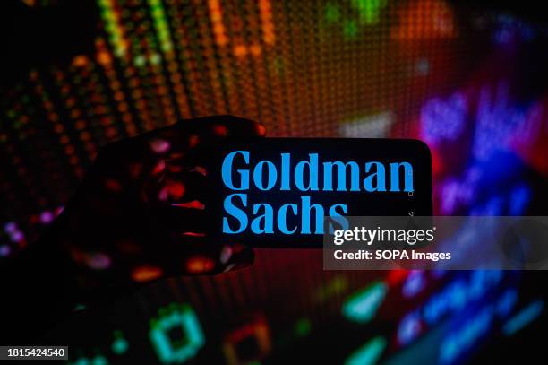 In this photo illustration, a Goldman Sachs logo is displayed on a smartphone with stock market percentages in the background.