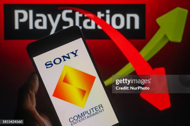 The Sony Interactive Entertainment logo is being displayed on a smartphone with a PlayStation and a stock graph visible in the background, in this...