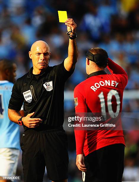 Referee Howard Webb shows a yellow card to Wayne Rooney of Manchester United during the Barclays Premier League match between Manchester City and...