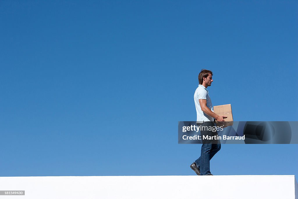 Man walking with cardboard box outdoors with blue sky