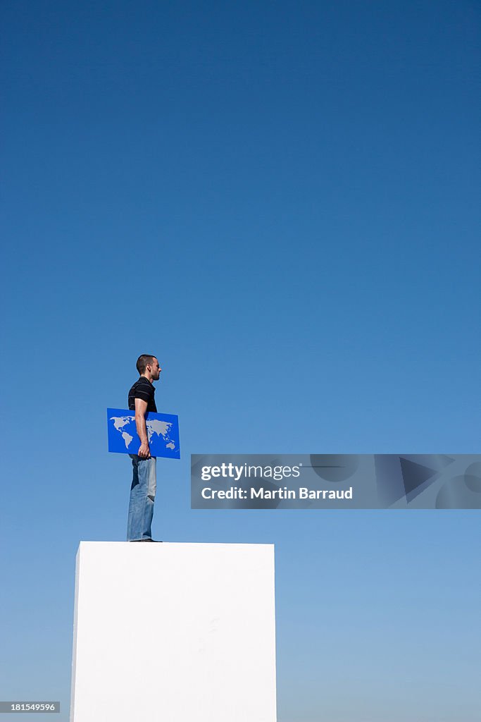 Homem de pé em pedestal ao ar livre com o mapa do mundo