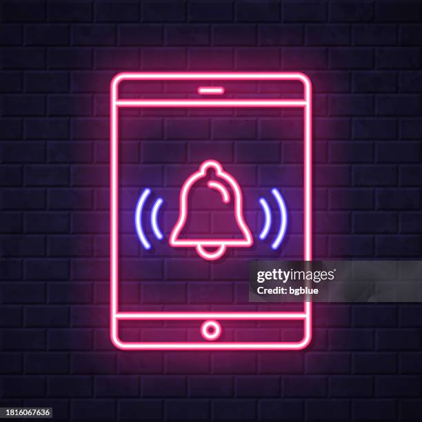 tablet pc with ringing bell - notification. glowing neon icon on brick wall background - notification bell stock illustrations