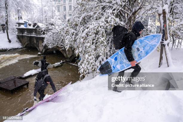 December 2023, Bavaria, Munich: Two men carry their surfboards up the embankment at the Eisbach in the English Garden. Photo: Peter Kneffel/dpa