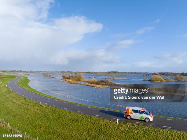 PostNL postal service Volkswagen ID.Buzz delivery van driving on a levee along the lflooded river IJssel due to high water levels on the floodplains...